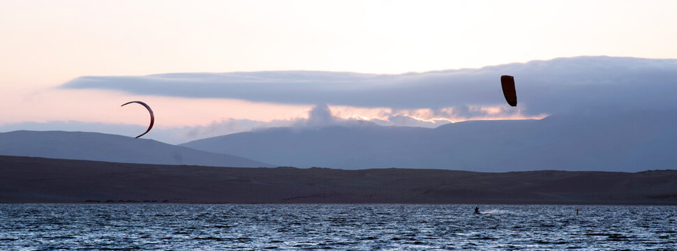 young people kitsurfing in a paracas bay of peru with blue water and drops in the air and mountains in the background-june 2020