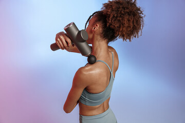 Woman use massage gun machine rehab after muscle workout standing on studio background