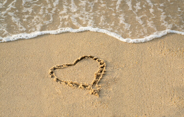 Heart shape on the sand of a beach with wave foam at the background. Copy space.