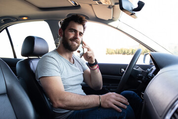 young man smiling and making a call on his phone, sitting on driver's seat, app driver calling user