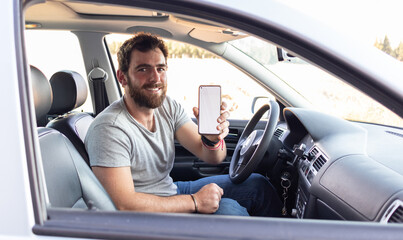 young man smiling showing the screen his phone, sitting on driver's seat, app driver calling user