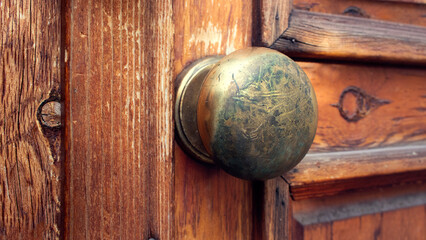 golden doorknob with dirty, scratched and rusty texture with an old wooden door in the background - closeup symbol of the entrance to a house