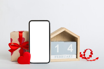 mobile phone with blank screen on colored background with hearts, calendar and gift box, valentine day 14 february concept perspertive view flat lay