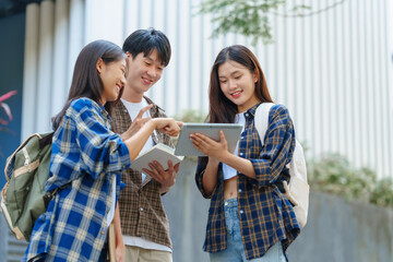 Attractive asian college student using laptop and tablet studying with group of friends together...