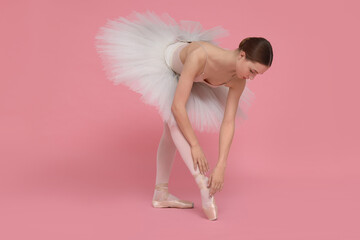 Young ballerina practicing dance moves on pink background