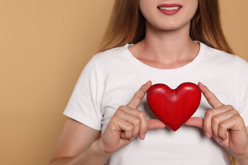 Young woman holding red heart on beige background, closeup with space for text. Volunteer concept