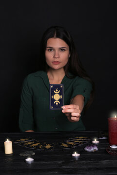 Soothsayer predicting future at table against black background, closeup. Focus on tarot card