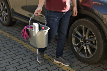 Man holding bucket with car cleaning products outdoors, closeup