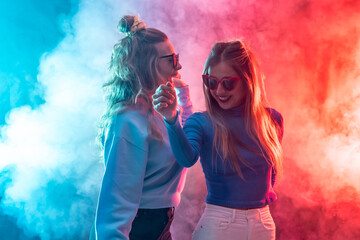 Two young blonde caucasian women dancing in nightclub, dancing having fun at party, red and blue...