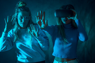 Two futuristic women in vr glasses, playing a game from virtual reality or the metaverse, blue background
