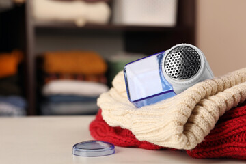 Modern fabric shaver and knitted clothes on white table indoors, closeup. Space for text
