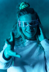 Obraz na płótnie Canvas Woman with futuristic glasses gesturing against a blue background, glasses for the metaverse