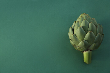 Whole fresh raw artichoke on green background. Space for text