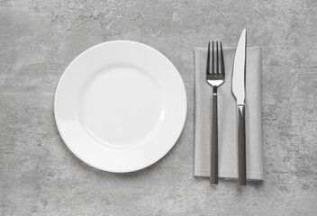Clean plate and shiny silver cutlery on light grey table, flat lay
