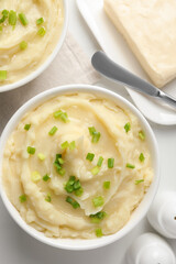 Bowls of delicious mashed potato with green onion on white table, flat lay