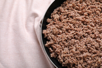 Fried minced meat in pan on table near kitchen napkin, top view. Space for text