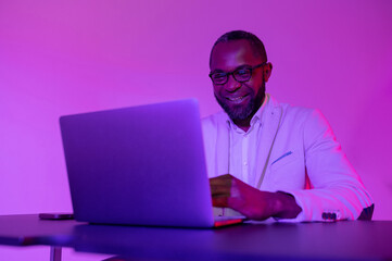 Man smiling at the computer at work. A black programmer works using a laptop computer. the man works at night.