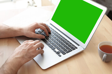Young man using laptop at desk, closeup. Device display with chroma key