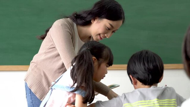 Asian school teacher using digital device with children in classroom at school, technology, learning, development.