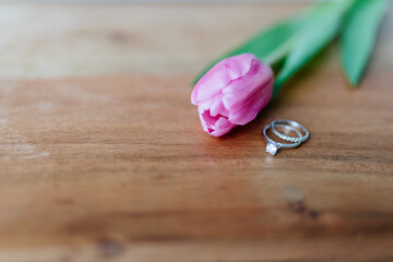 Obraz na płótnie Canvas Pink tulip and a ring with a diamond lies on a wooden background. Background for Valentine's Day