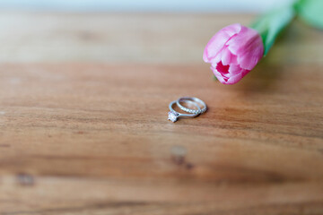Pink tulip and a ring with a diamond lies on a wooden background. Background for Valentine's Day