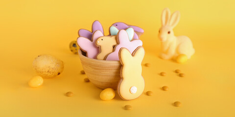 Bowl with tasty Easter cookies in shape of bunny on yellow background