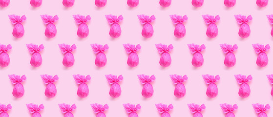 Many chocolate Easter eggs wrapped in pink paper on color background. Pattern for design