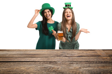 Happy young women with beer near table on white background. St. Patrick's Day celebration