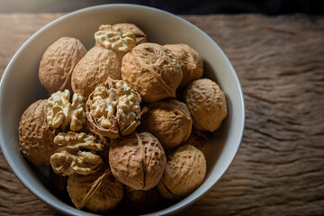 Raw brown organic walnut kernels with shell in a bowl on rustic wooden table.