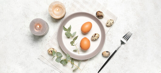 Table setting with Easter eggs and candles on light background