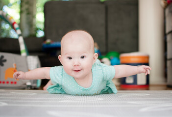 Infant baby girl on the floor during tummy time with her arms up like flying