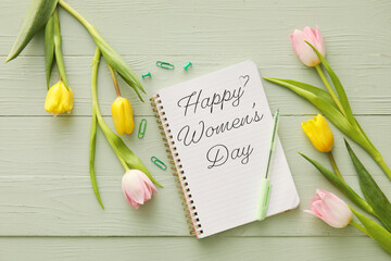 Notebook with text HAPPY WOMEN'S DAY and beautiful flowers on color wooden background