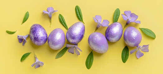 Beautiful Easter eggs and flowers on yellow background