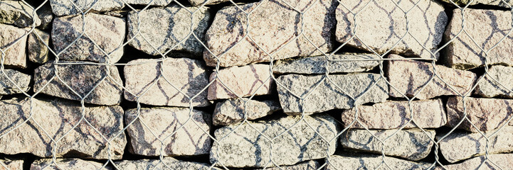 Wall of stones held by a metal mesh. Wide panoramic texture for background and design.