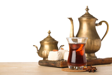 Cup of Turkish tea, teapot, sugar bowl and sweets on wooden table against white background