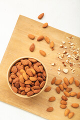 Wooden board with bowl of almond nuts on light background, closeup