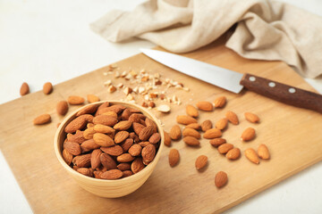 Wooden board with bowl of almond nuts on light background, closeup