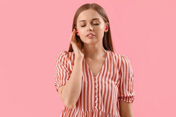 Young woman with ear plugs on pink background