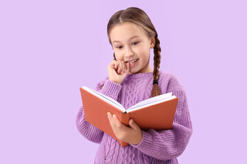 Little girl biting nails while reading book on lilac background
