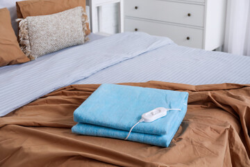Folded electric heating pad with controller on bed in room, closeup