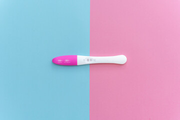Flat lay of pregnancy test kit with two stripes. Pastel pink and blue color background. Positive result. Closeup. Point of view shot. 