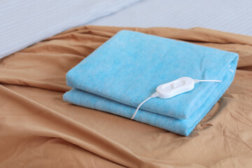 Folded electric heating pad with controller on bed in room, closeup