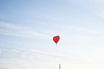 Fototapeta premium A colorful balloon in the shape of a heart, flying at sunset across the blue sky. Happy Valentine's Day Concept. space for text.