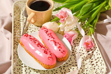 Tray with delicious eclairs and flowers on light background