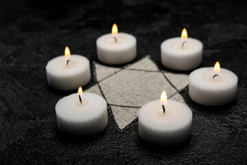 Fototapeta na wymiar Burning candles and Jewish badge on dark background. International Holocaust Remembrance Day