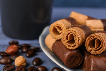 Plate of delicious wafer rolls with coffee beans and hazelnuts on blue background
