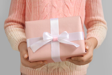 Woman in sweater with gift box for Valentine's Day on grey background, closeup