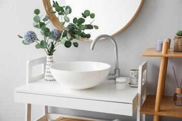 Sink, vase with flowers and eucalyptus on table in bathroom