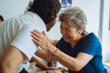 Fototapeta premium Latin grandson greeting his grandmother at a family reunion through a hug.
