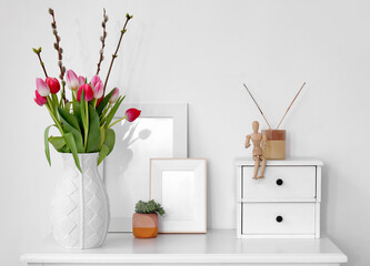 Vase with tulips, willow branches and frames on table in living room